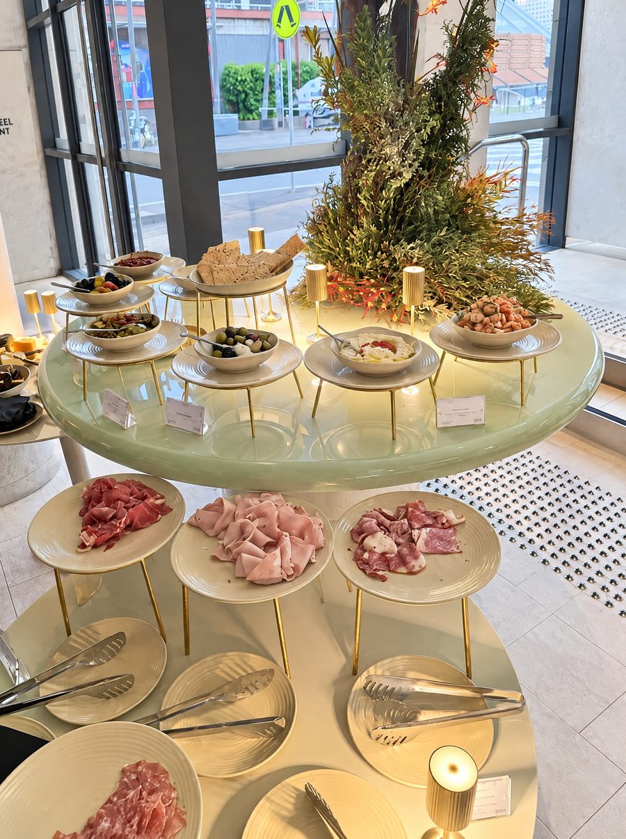 Adina Sydney Darling Harbour, grazing station of cured meats, cheeses and olives on tiered stands beside a native flower arrangement at a street facing window
