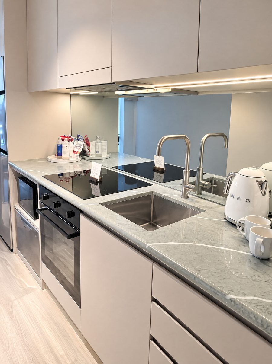 Adina Sydney Darling Harbour, kitchen with an induction cooktop, an oven, a microwave and a stone benchtop, a white kettle and mugs beside the sink