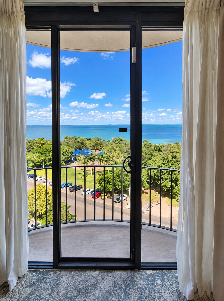 DoubleTree by Hilton Esplanade Darwin, glass door opening onto a curved balcony, looking over parkland and the Esplanade to the harbour